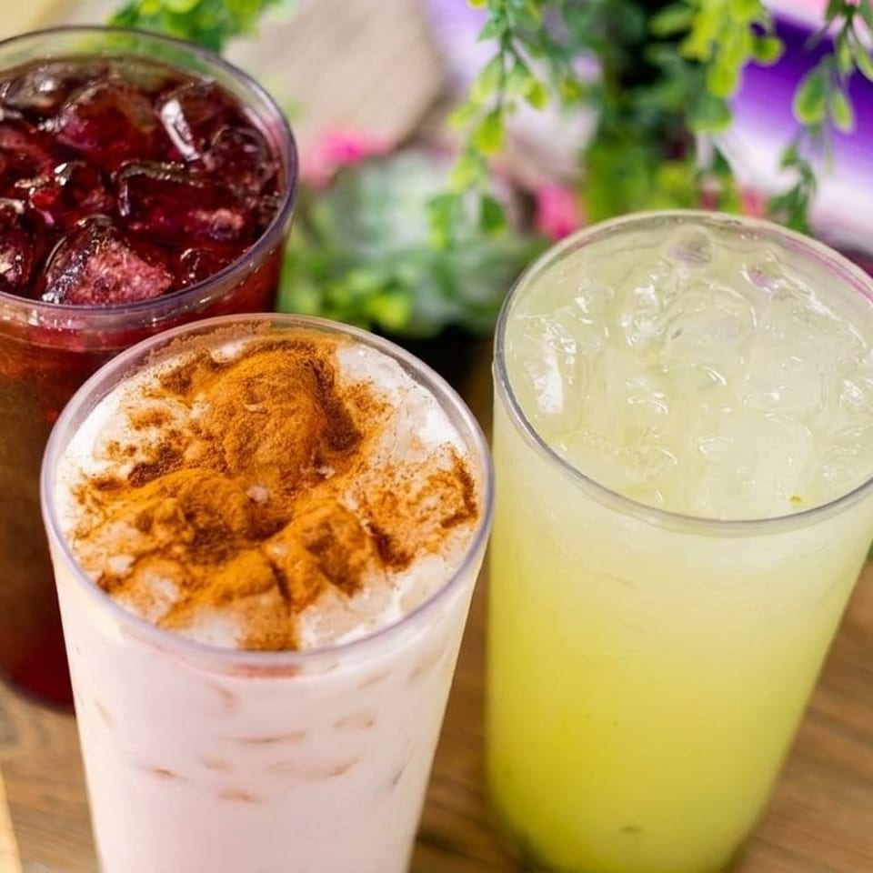 Three refreshing drinks: red, horchata with cinnamon, and light green, on a wooden surface.