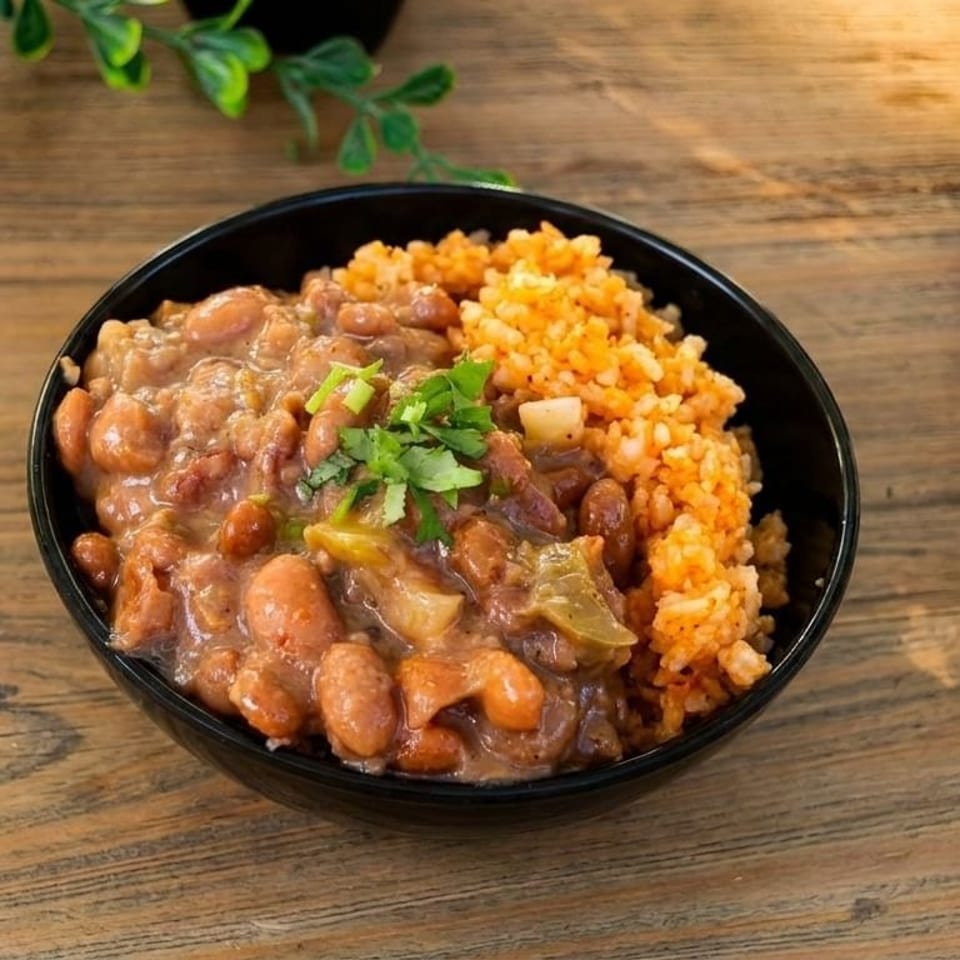 A black bowl filled with pinto beans and red rice, garnished with cilantro on a wooden table.