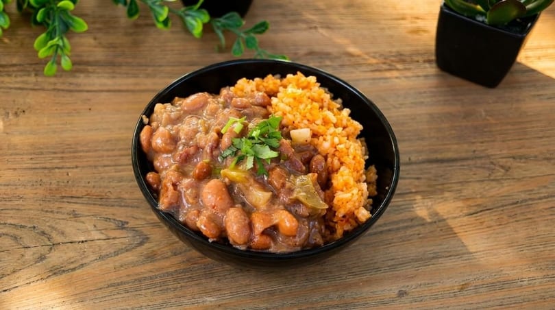 A black bowl filled with pinto beans and red rice, garnished with cilantro on a wooden table.