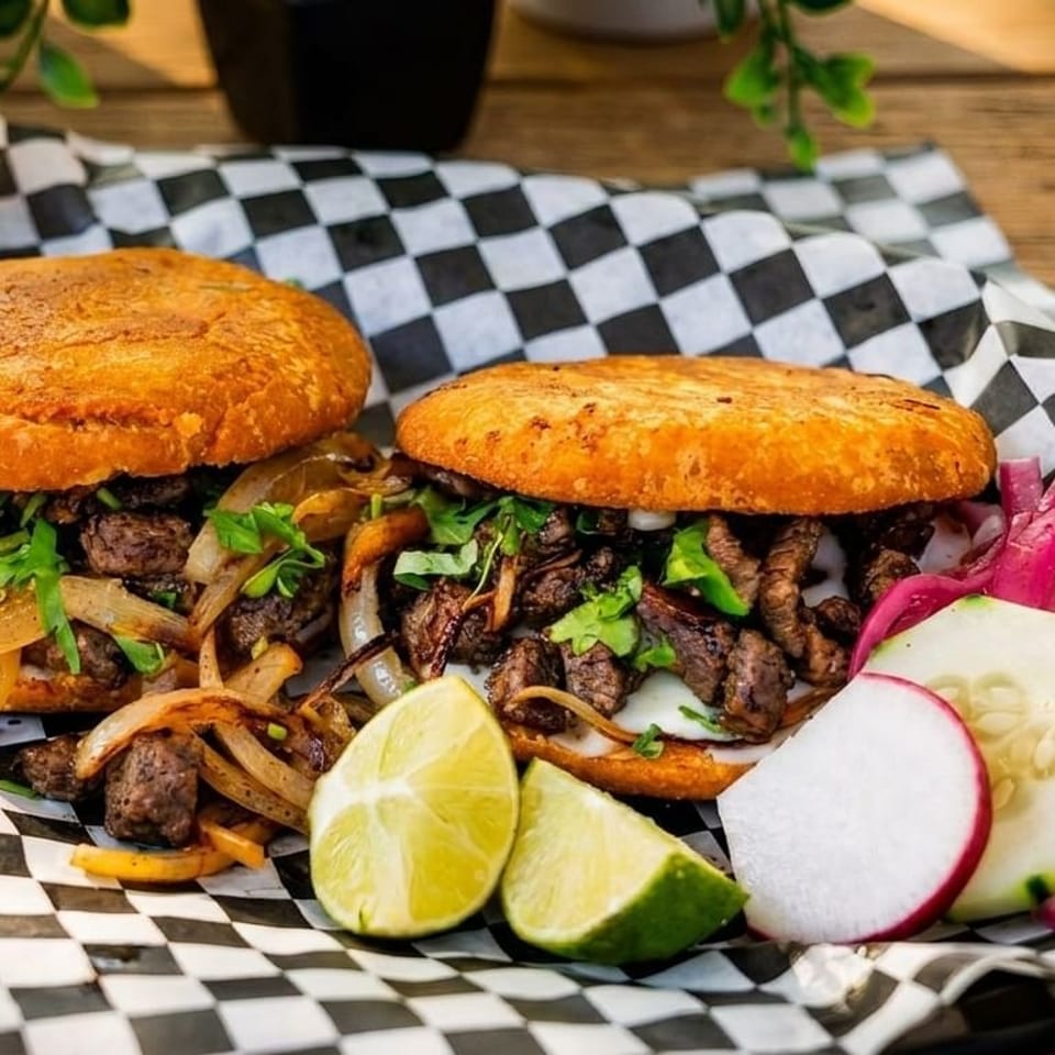 Two arepas filled with steak, onions, and cilantro, served with lime, radishes, and pickled onions.