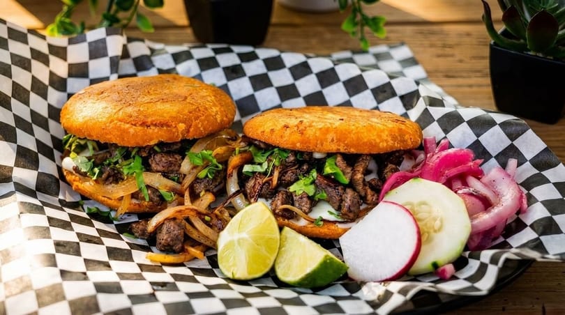 Two arepas filled with steak, onions, and cilantro, served with lime, radishes, and pickled onions.